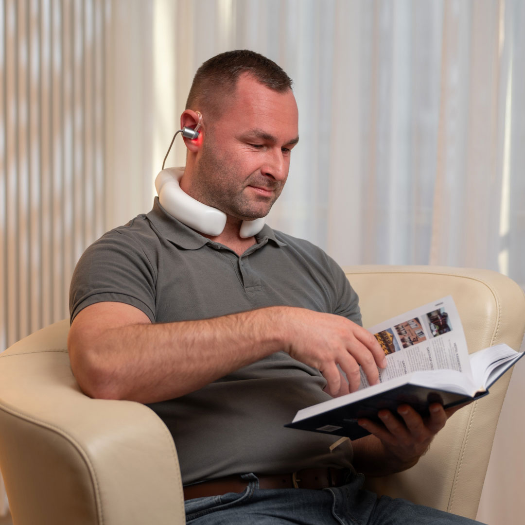 Mann sitzt entspannt im Wohnzimmer und nutzt den LumoHome Laser zur sanften Anwendung am Innenohr.“