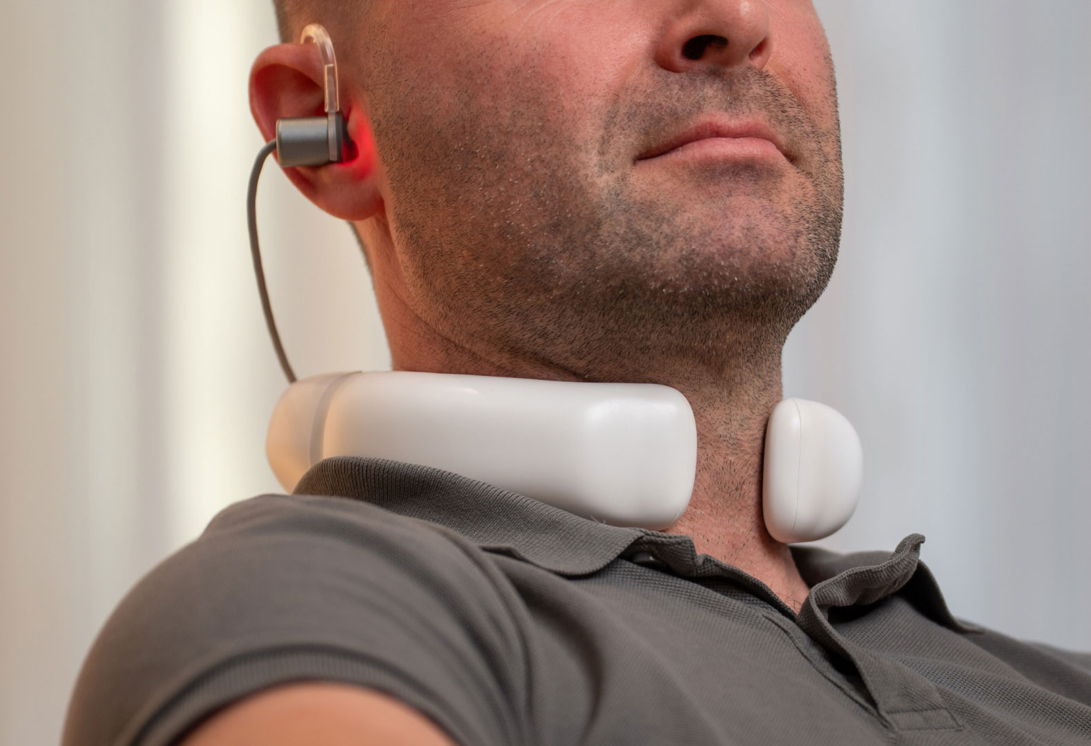 Mann sitzt entspannt im Wohnzimmer und nutzt den LumoHome Laser zur sanften Anwendung am Innenohr.“